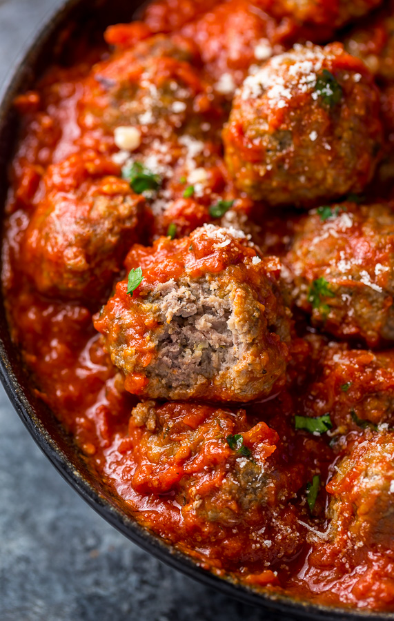 Meatballs with tomato sauce and parmesan cheese in a black bowl.