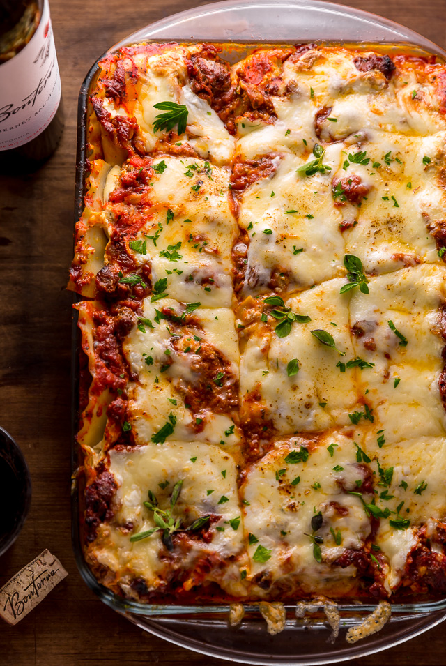 Casserole dish full of lasagna with red wine on the side.