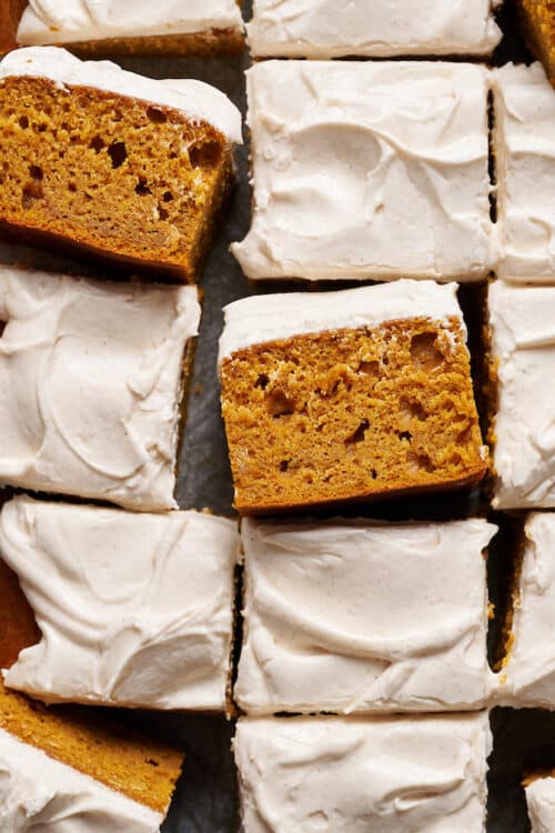 Pumpkin cake topped with cream cheese frosting sliced into squares.